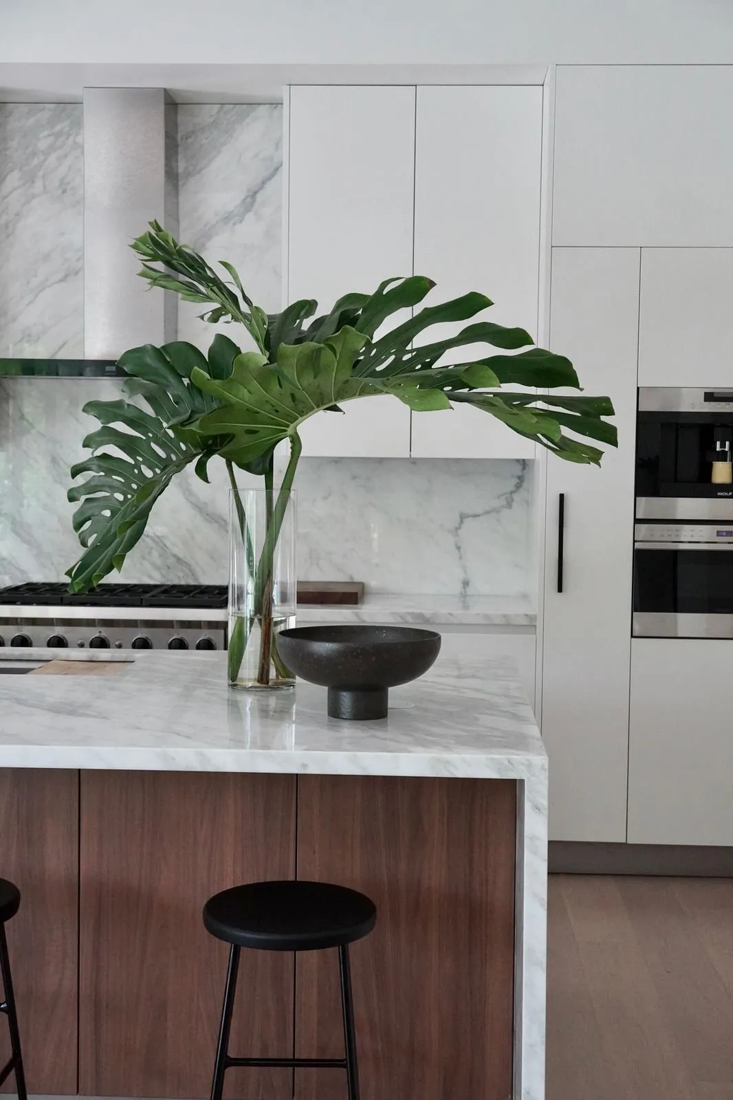 Marble-topped kitchen island with a monstera plant and black stools, G Residence remodel by DALOP Design