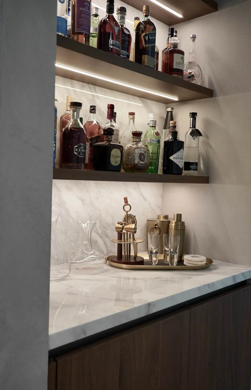 Backlit home bar shelving in marble with glassware and spirits, a contemporary bar by DALOP Design