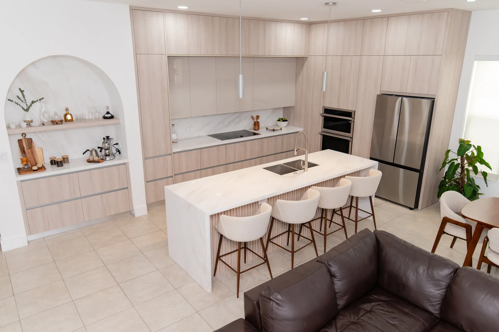JH Residence kitchen by DALOP Design: pale oak cabinetry, a marble island with white stools and an arched doorway to the living room