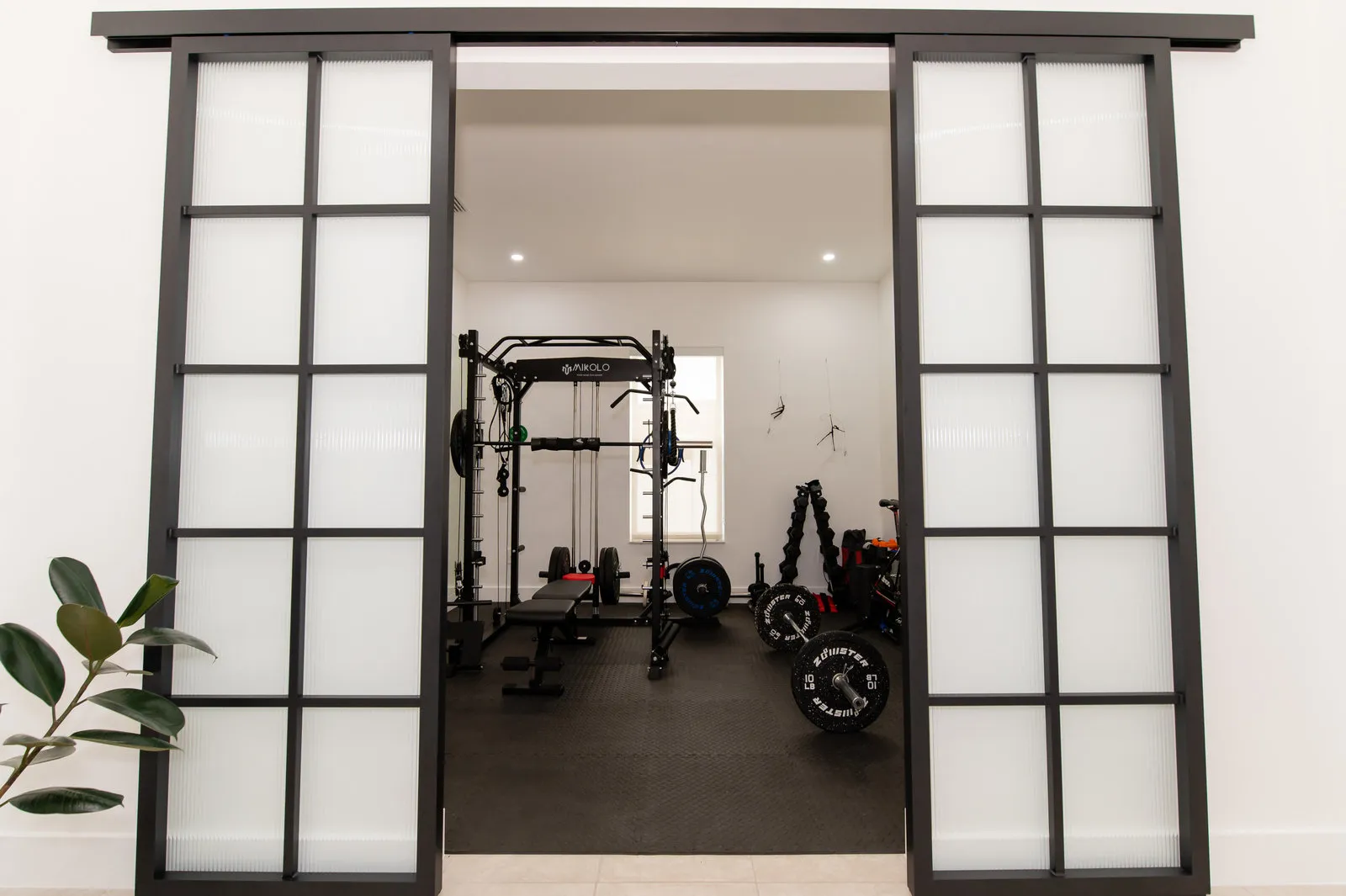 Black steel-framed glass doors opening onto a home gym, JH Residence secondary rooms