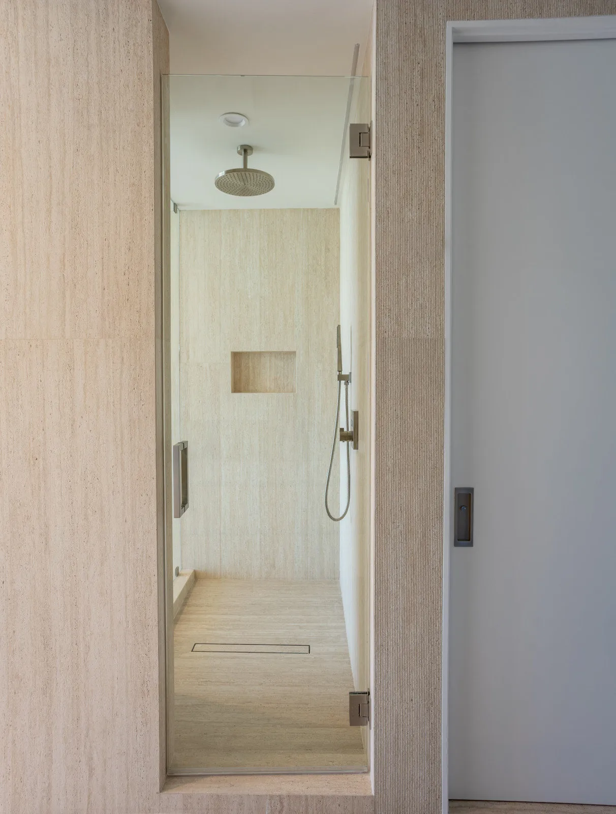 Travertine-clad shower with a rain head and a floating oak vanity, Marquis renovation by DALOP Design
