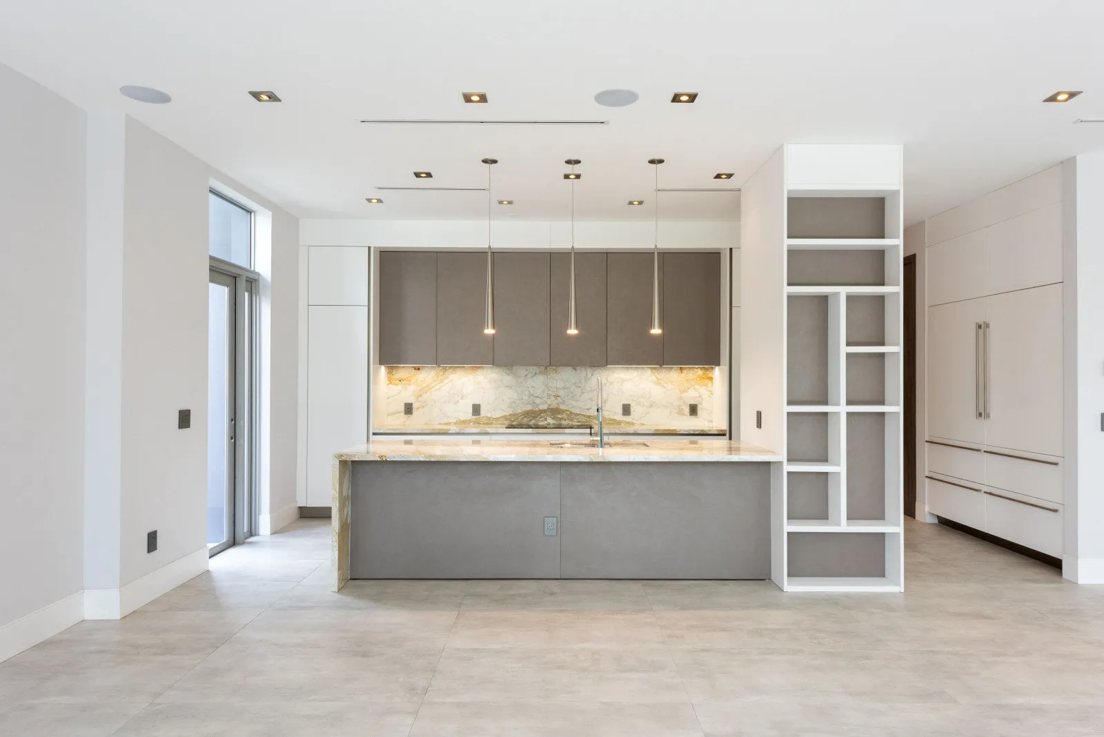 White kitchen with a grey island and a wall of tall cabinetry in the Coral Gables spec home by DALOP Design